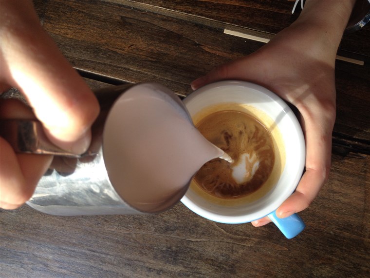 Menuangkan a dollop of steamed milk into espresso