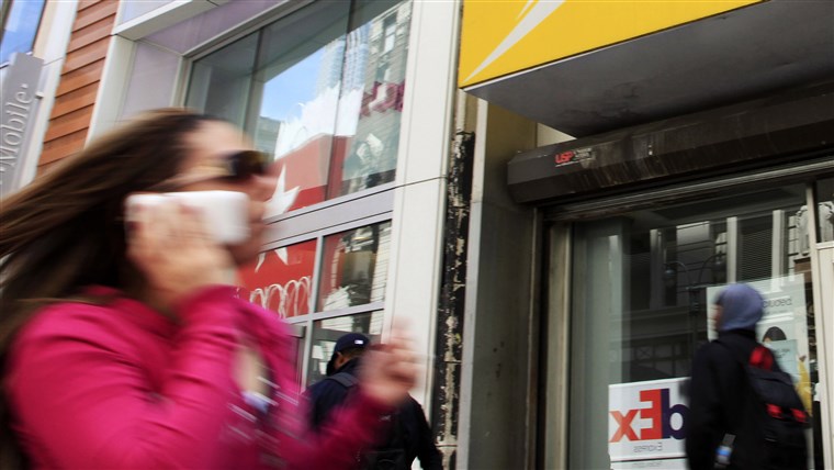 UN woman using a cell phone walks past T-Mobile and Sprint stores, Tuesday, April 27, 2010, in New York. Sprint Nextel Corp. on Wednesday, April 28, sa...