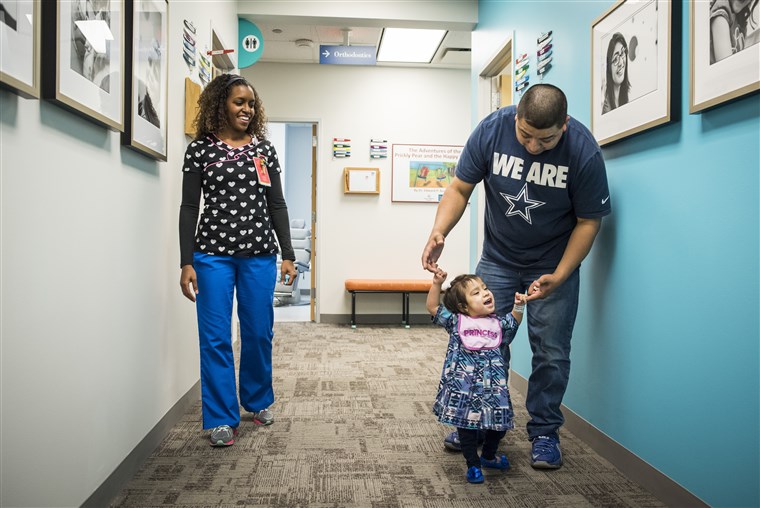 에릭 Mata holds daughter Knatalye’s hands as she walks down the hall of a clinic at Texas Children’s Hospital.
