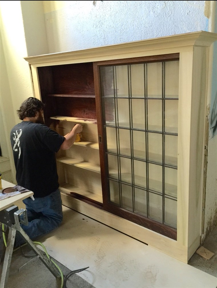 Aaron Gray, one of the Singing Contractors, paints wood stain onto cabinets he built.