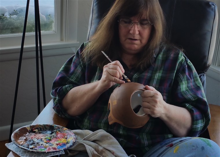 Digambar, 60, paints baby helmets from the living room of her Washington home.