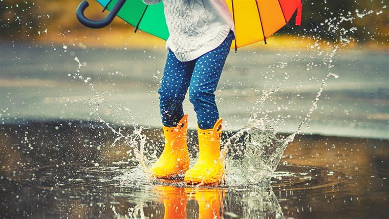 피트 of child in yellow rubber boots jumping over puddle in rain